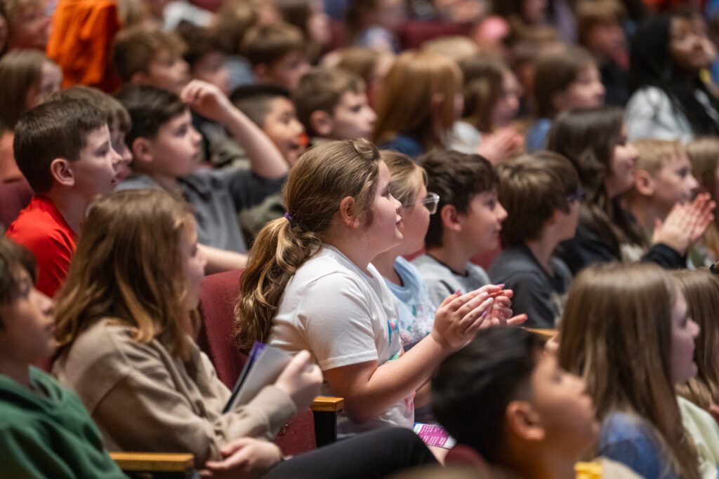 Children watch and applaud a performance in a theatre