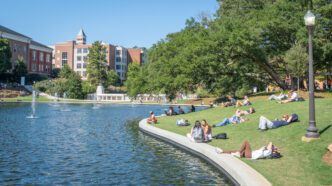 Students sit on the grass next to the newly filled reflection pond on a summer day.